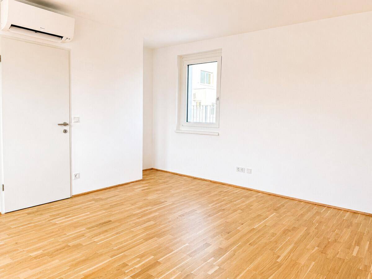 Geräumiges Schlafzimmer mit Parkettboden, Klimaanlage und einem großen Fenster.