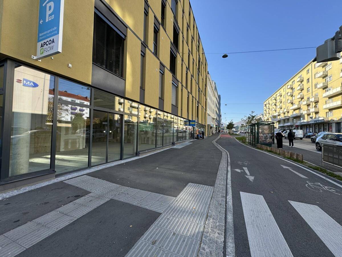 Ansicht der modernen Gebäudefassade entlang einer belebten Straße mit Fußgänger- und Radweg.