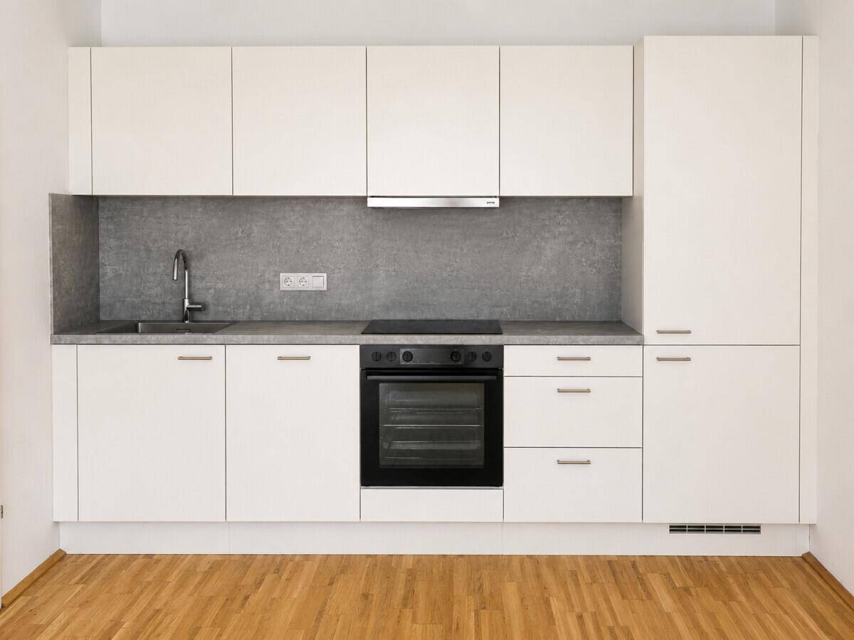 Detailansicht einer modernen, weißen Einbauküche mit grauer Arbeitsplatte und integrierten Geräten.