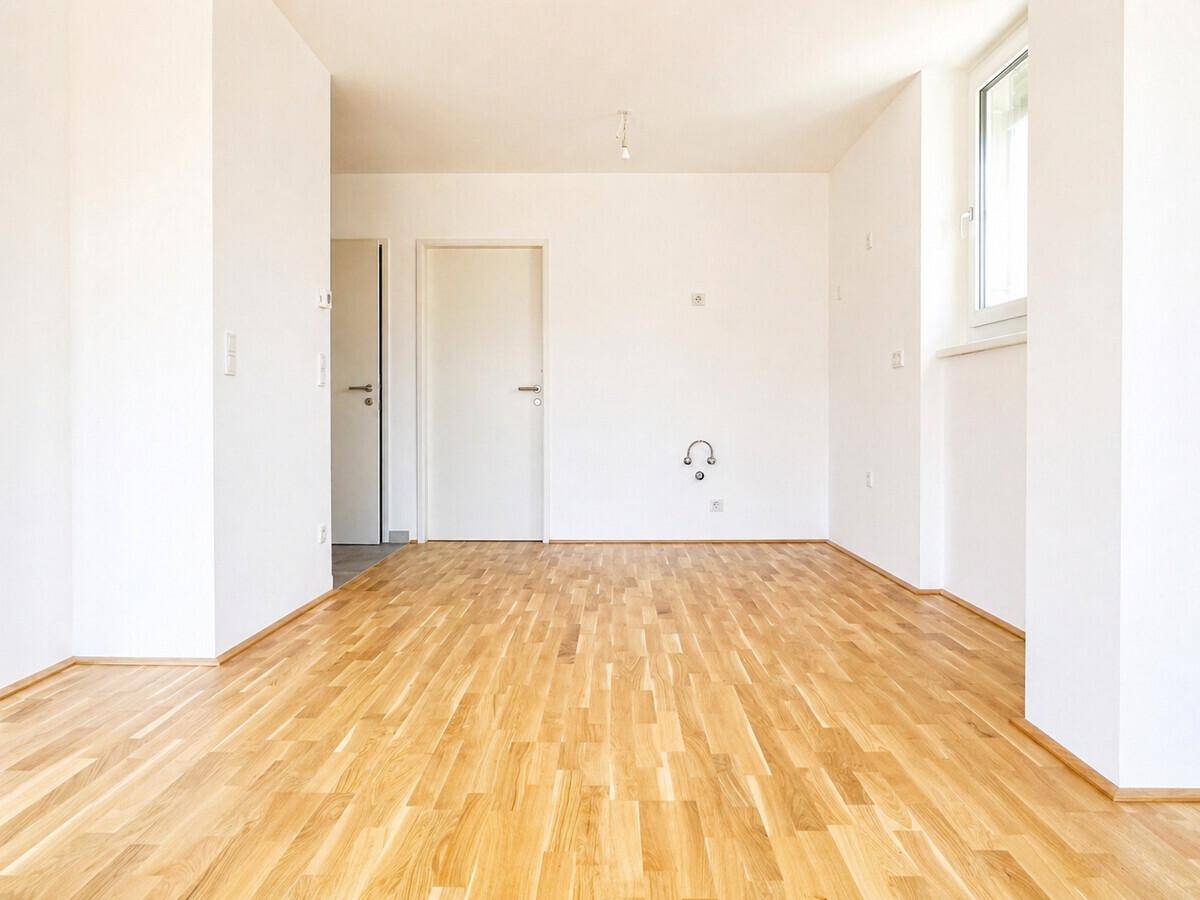Leerer Raum mit hellem Parkettboden, weißen Wänden und einer Tür, bereit zur individuellen Gestaltung.