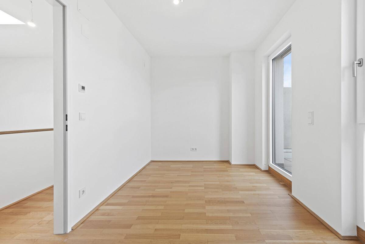 Helles, leeres Zimmer mit Parkettboden und großem Fenster, ideal als Schlaf- oder Arbeitszimmer.