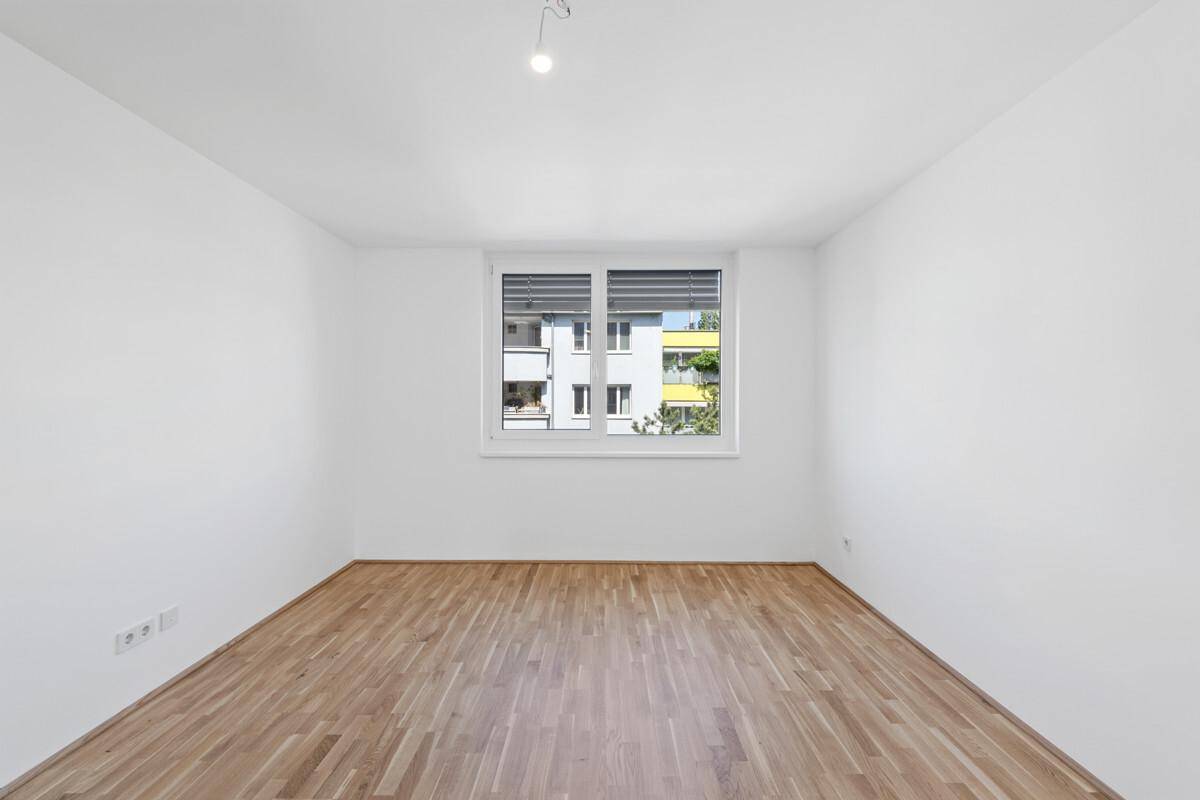 Leeres Zimmer mit Parkettboden und großem Fenster, gut geeignet als Schlaf- oder Arbeitszimmer.