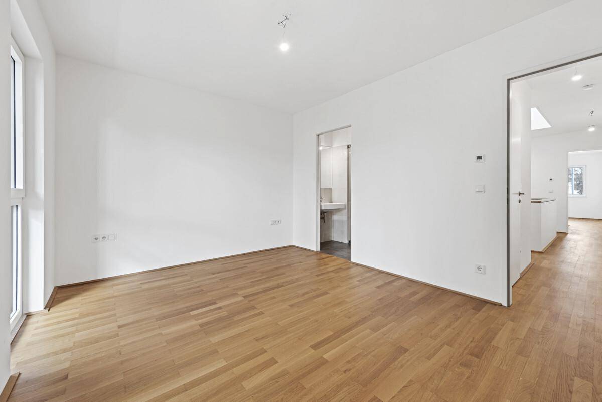 Geräumiges Zimmer mit Parkettboden und Blick in ein modernes Badezimmer.