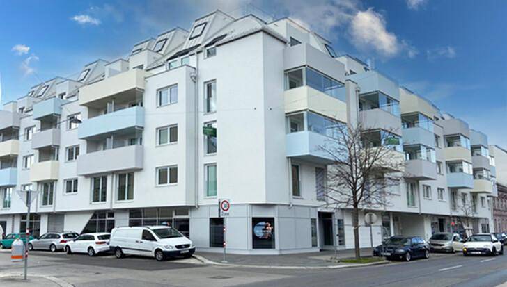 Modernes Wohngebäude mit weißer Fassade, vielen Balkonen und großen Fenstern an einer Stadtstraße.