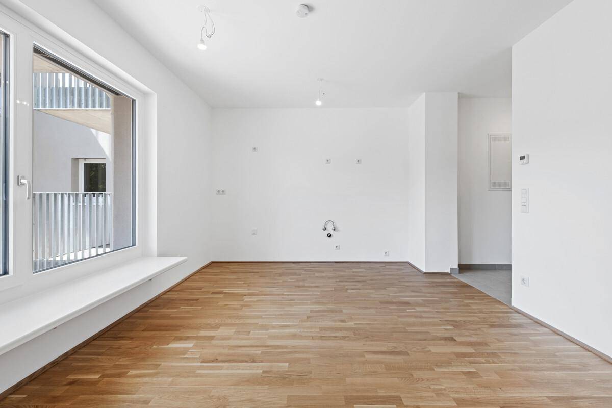 Geräumiges, leeres Zimmer mit hellem Parkettboden und Blick auf den Balkon.