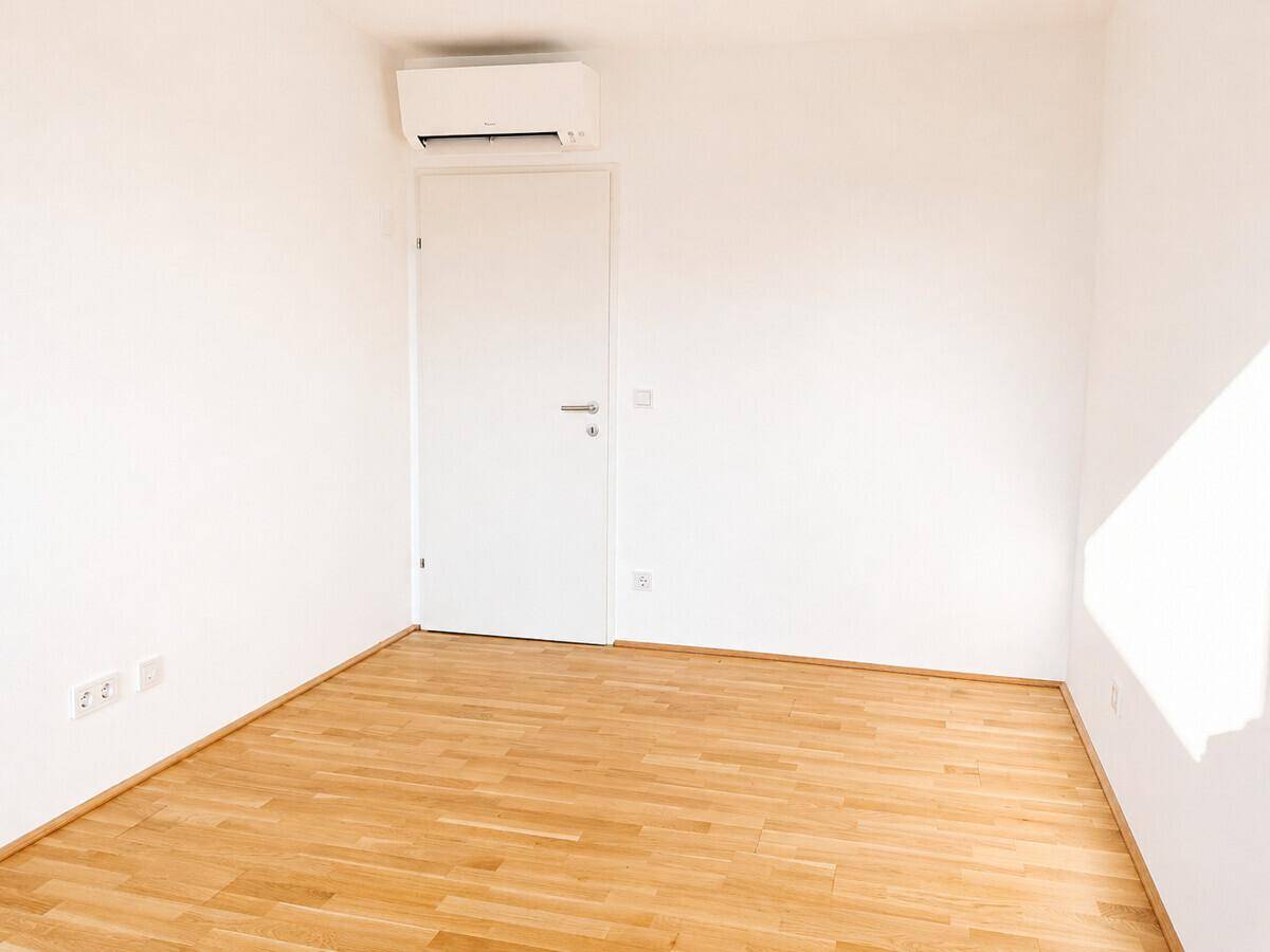 Leeres Schlafzimmer mit Parkettboden, Tür und Klimaanlage an der Decke.