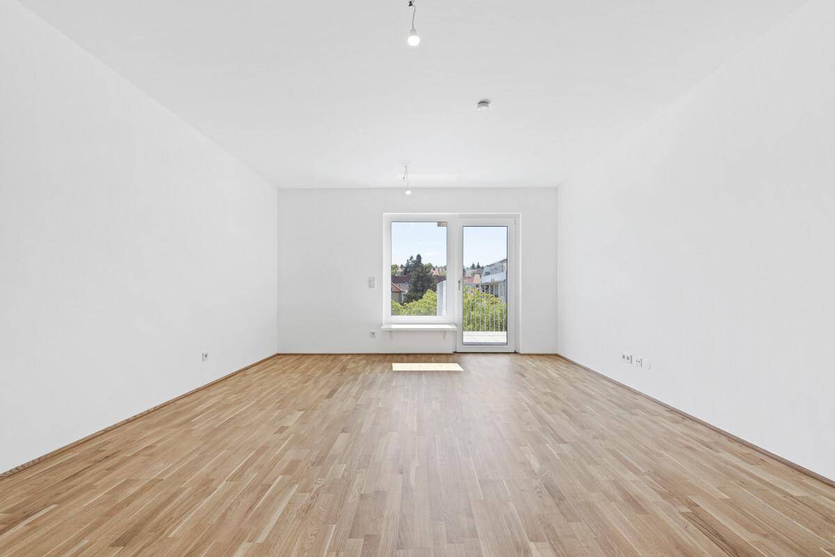 Heller, leerer Raum mit weiß gestrichenen Wänden und hochwertigem Parkettboden, mit Zugang zu einem Balkon.