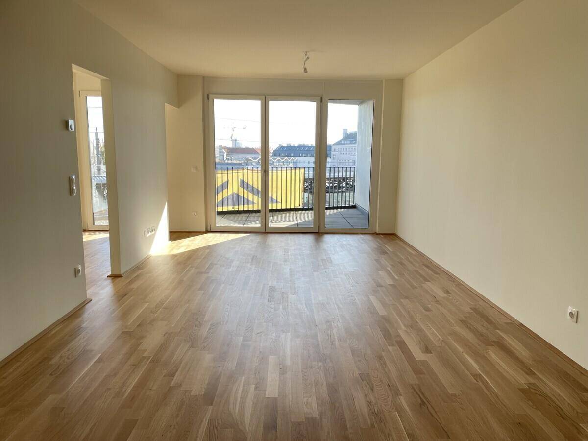 Heller Wohnraum mit Parkettboden und großen Schiebetüren, die zu einem sonnigen Balkon führen.