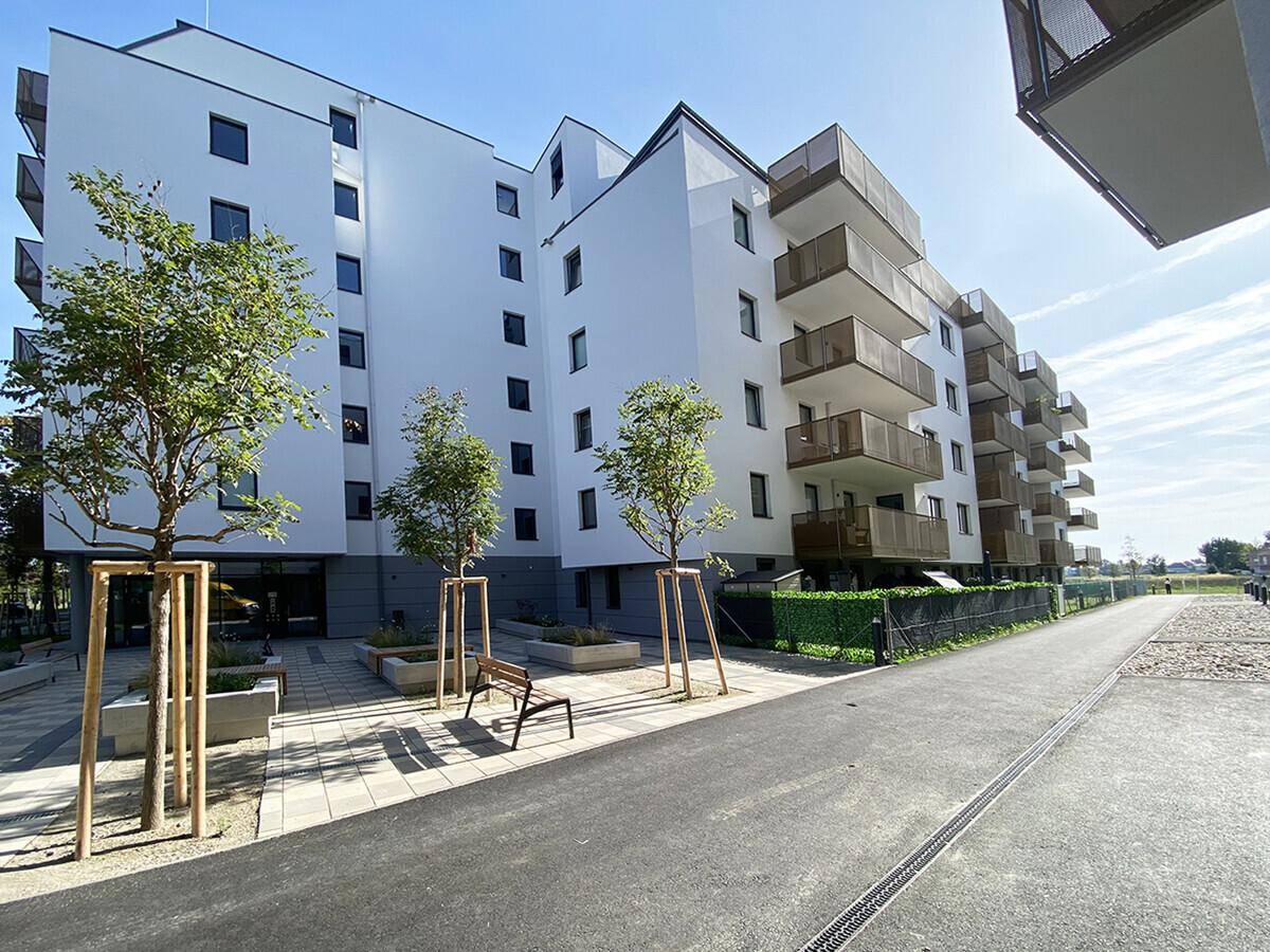 Moderne Wohnanlage mit weißer Fassade, zahlreichen Balkonen und gepflegten Außenbereichen unter blauem Himmel.
