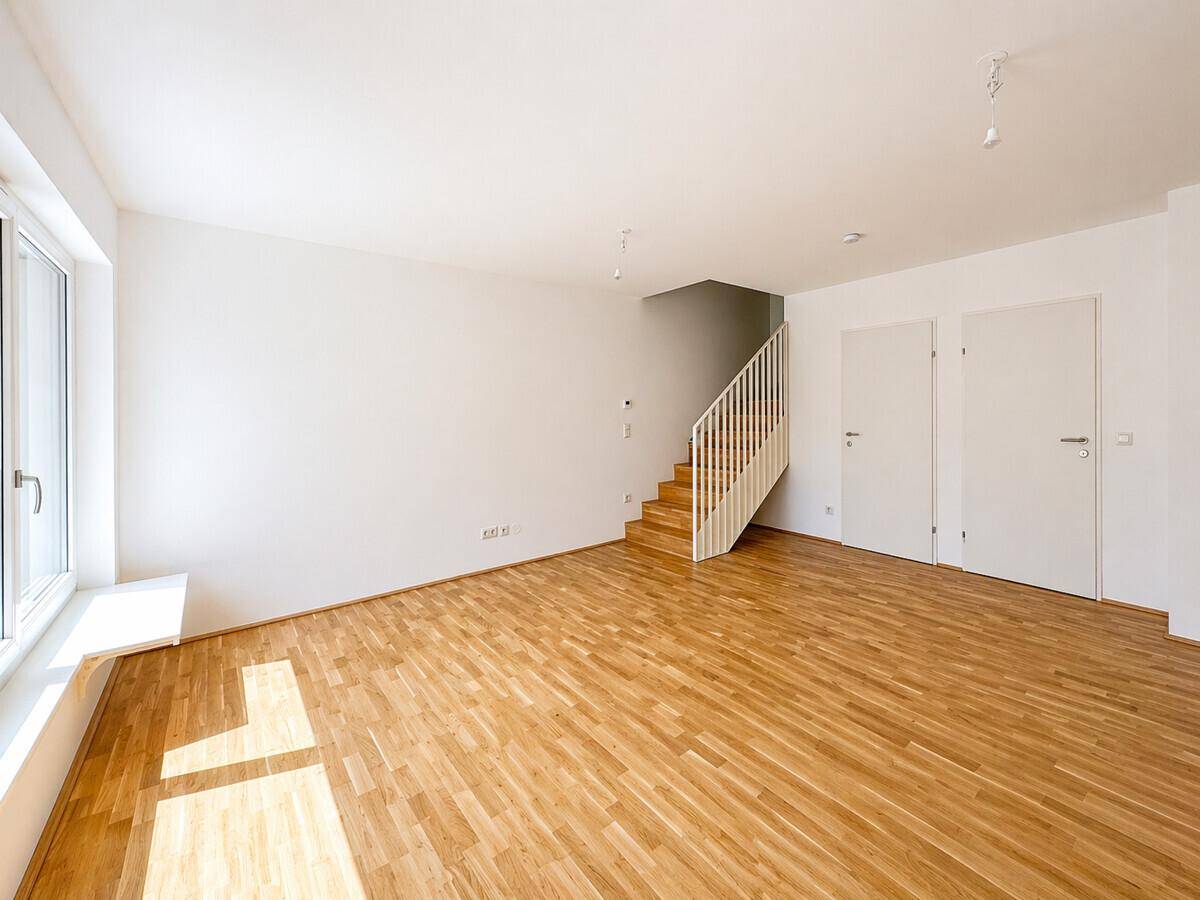 Geräumiges, helles Zimmer mit Holzparkett und einer Treppe, die in die obere Etage führt.