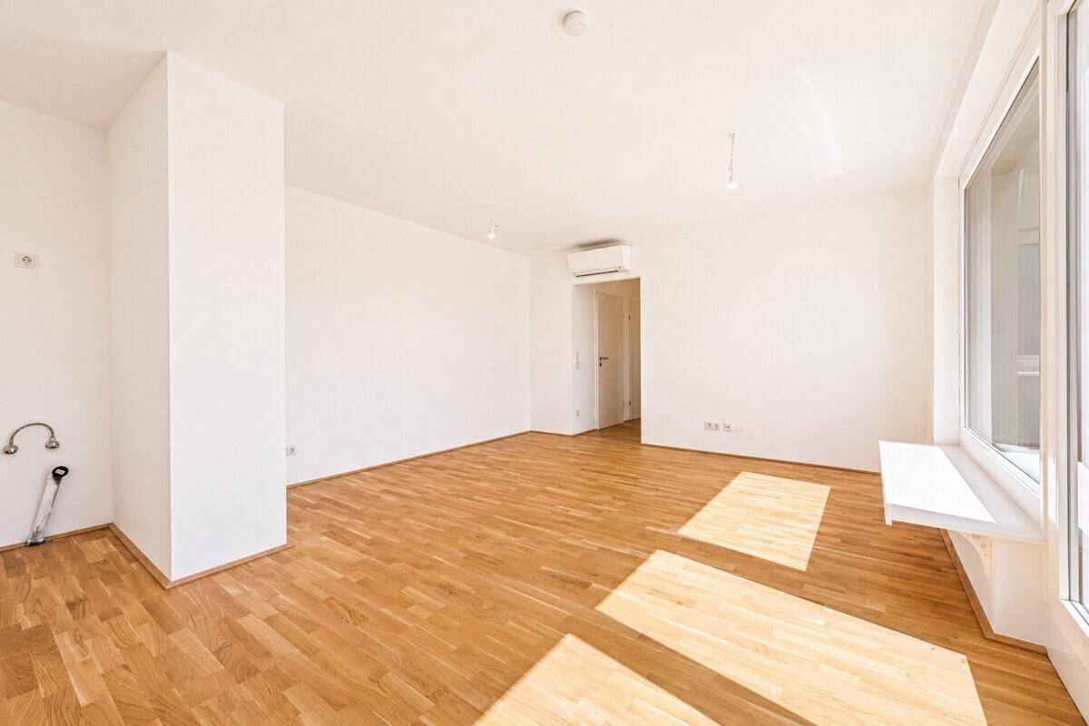 Heller, leerer Raum mit Parkettboden und Anschlüssen für eine Küche oder Waschmaschine, mit Fenster.