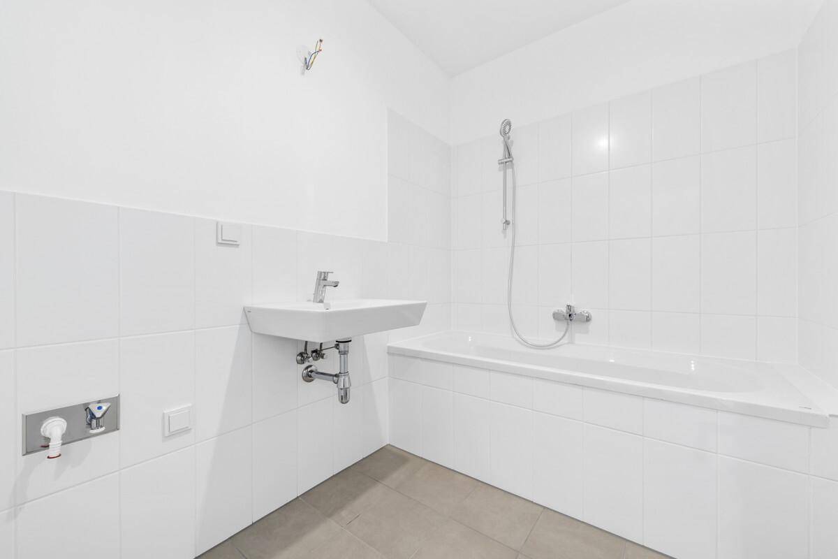 Unmöbliertes Badezimmer mit Badewanne und Waschbeckenanschluss, bereit für die Einrichtung.