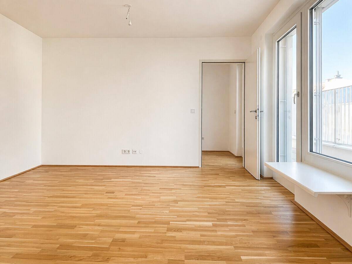 Geräumiges, helles Zimmer mit Holzboden und einer Tür, die zu einem weiteren Bereich führt.
