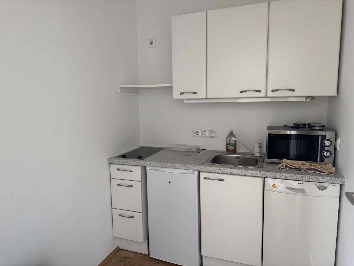 Kleine, funktionale Küchenzeile mit weißen Schränken, Spüle, Kochfeld und integrierten Geräten.