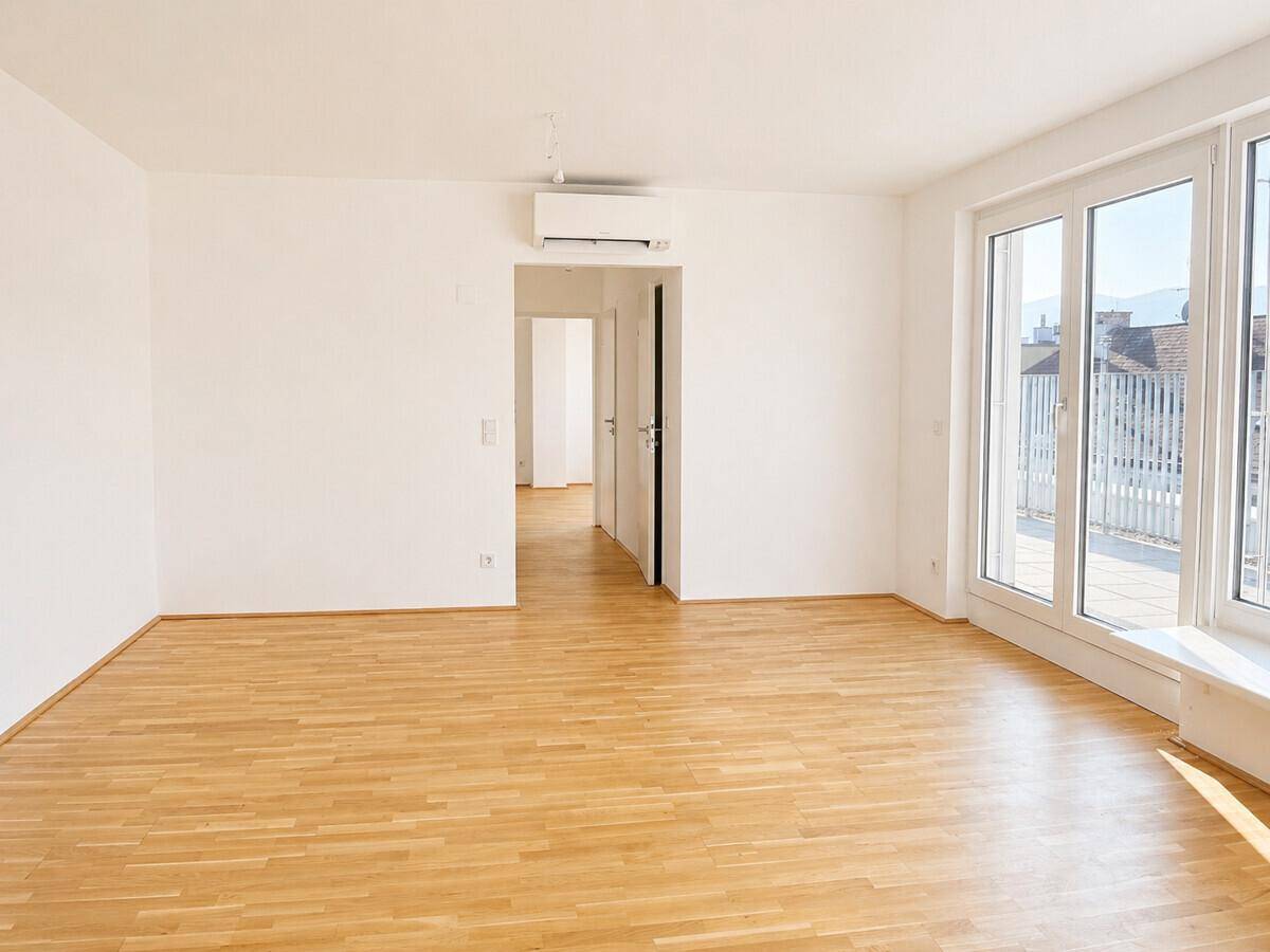 Geräumiger, heller Wohnbereich mit Holzparkett, Klimaanlage und Blick in den Flur.