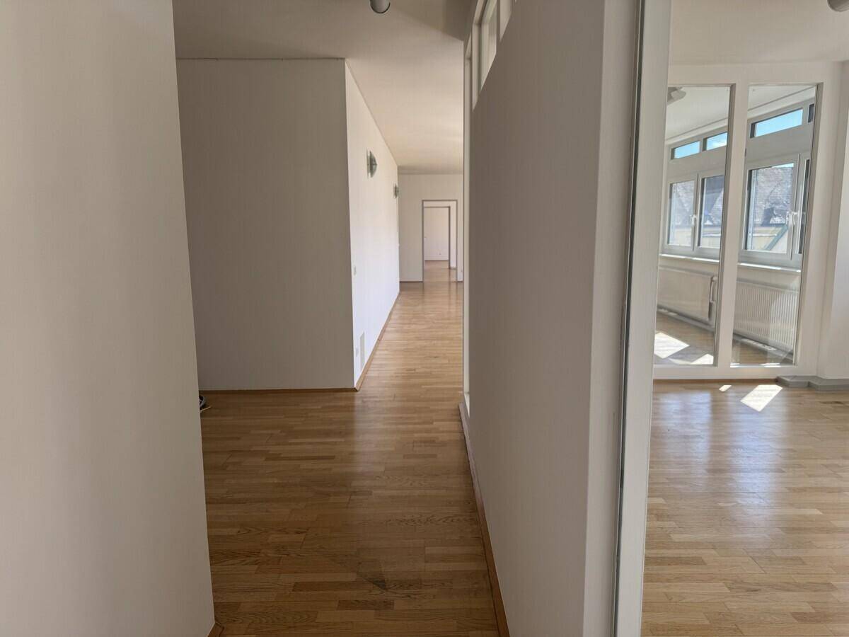 Langer, heller Flur mit Parkettboden und weißen Wänden, der verschiedene Bereiche des Gebäudes miteinander verbindet.