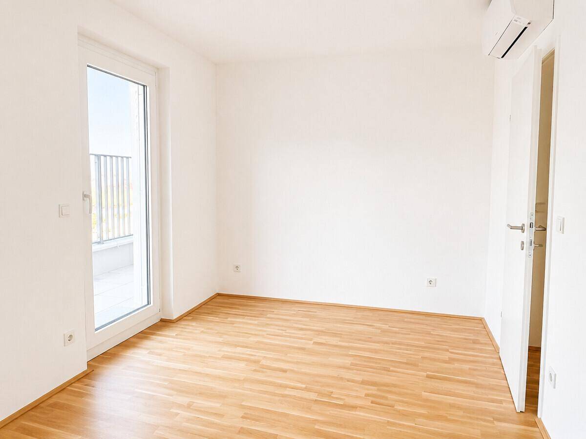 Unmöbliertes Schlafzimmer mit Parkettboden, Klimaanlage und Zugang zu einem Außenbereich.