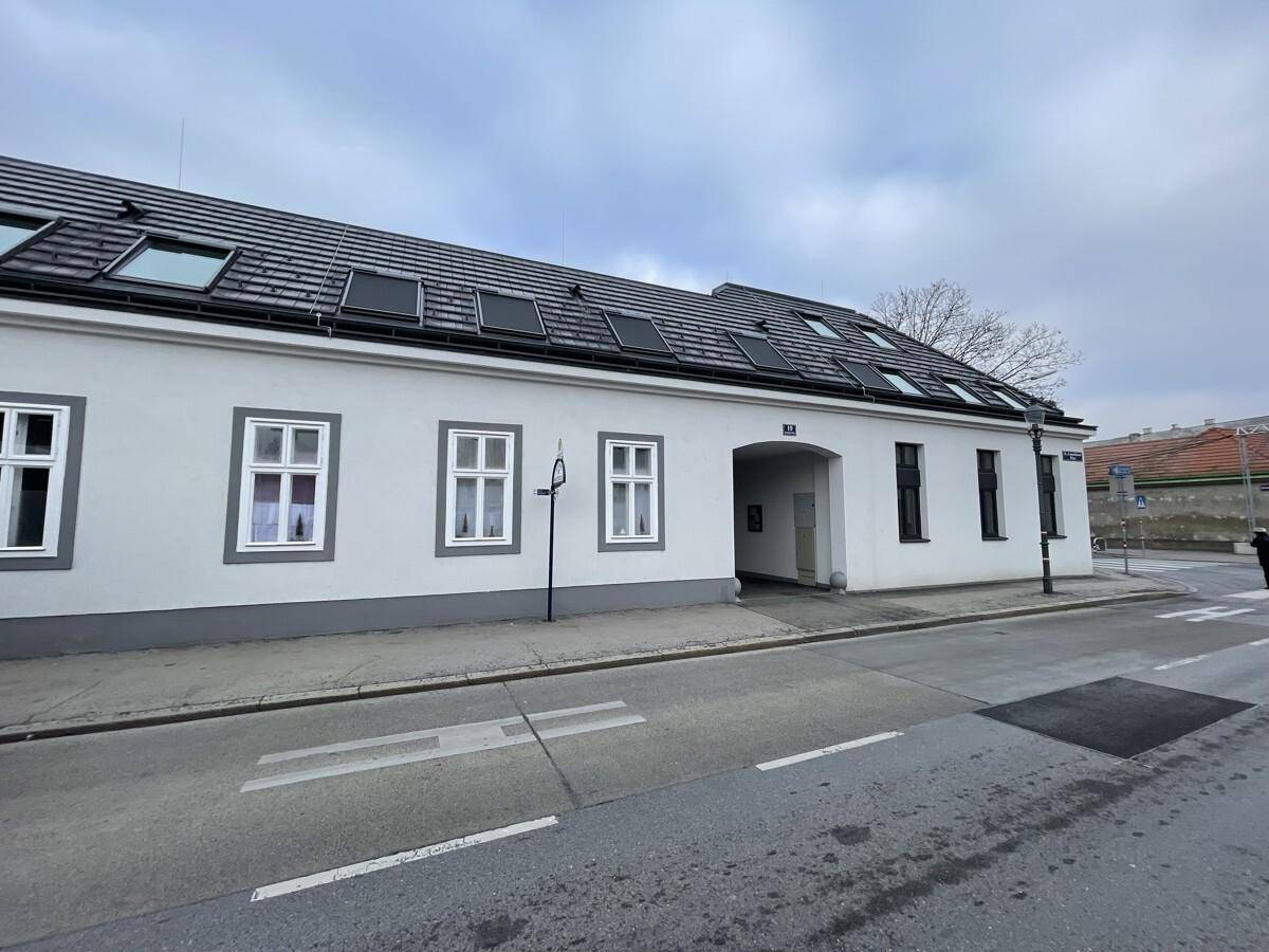 Straßenansicht eines langen, weißen Gebäudes mit verschiedenen Fenstertypen und Dachfenstern.
