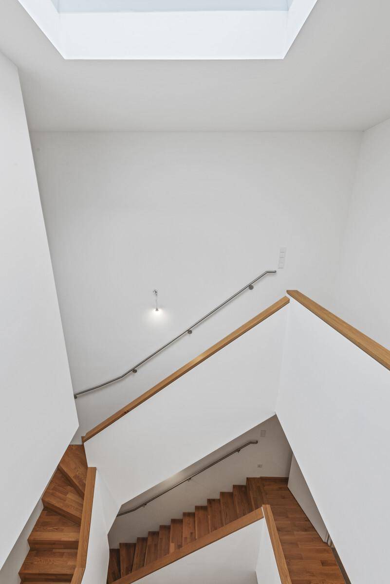 Moderner Treppenaufgang mit Holzstufen und viel Tageslicht durch das Oberlicht.