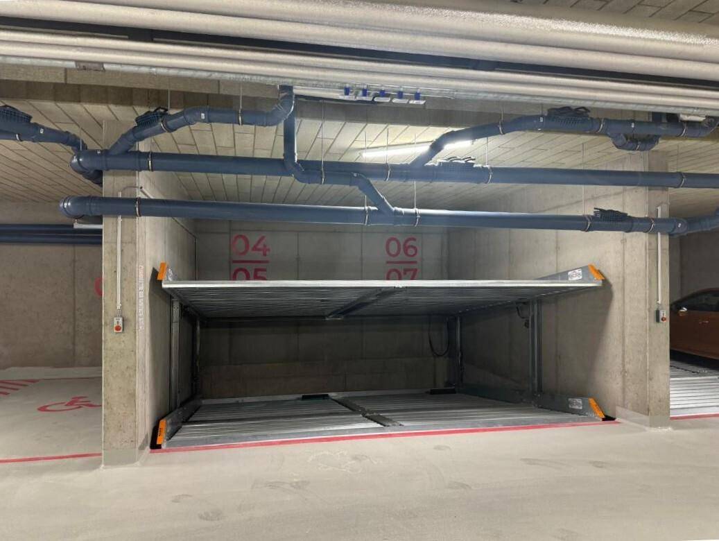 Tiefgarage mit modernem Doppelparker-System und sichtbaren Versorgungsleitungen an der Decke.
