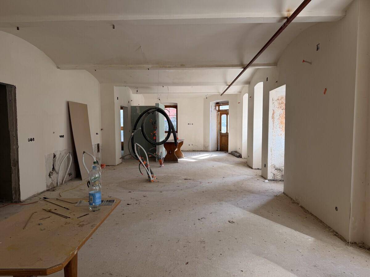 Weitläufiger Renovierungsraum mit unfertigen Wänden, sichtbaren Leitungen und einem provisorischen Tisch in der Mitte des Raumes.