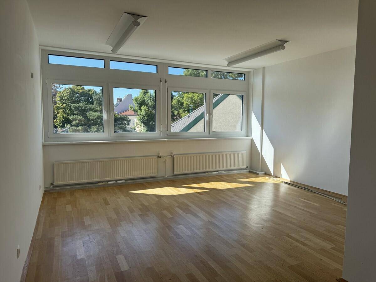 Heller Büroraum mit Holzboden und großen Fenstern, die viel Tageslicht und einen Blick ins Grüne bieten.