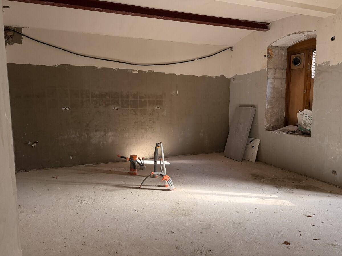 Teilansicht eines Raumes im Rohbau mit vorbereiteten Wänden, einem Fenster und einem sichtbaren Deckenbalken, der Tageslicht hereinlässt.