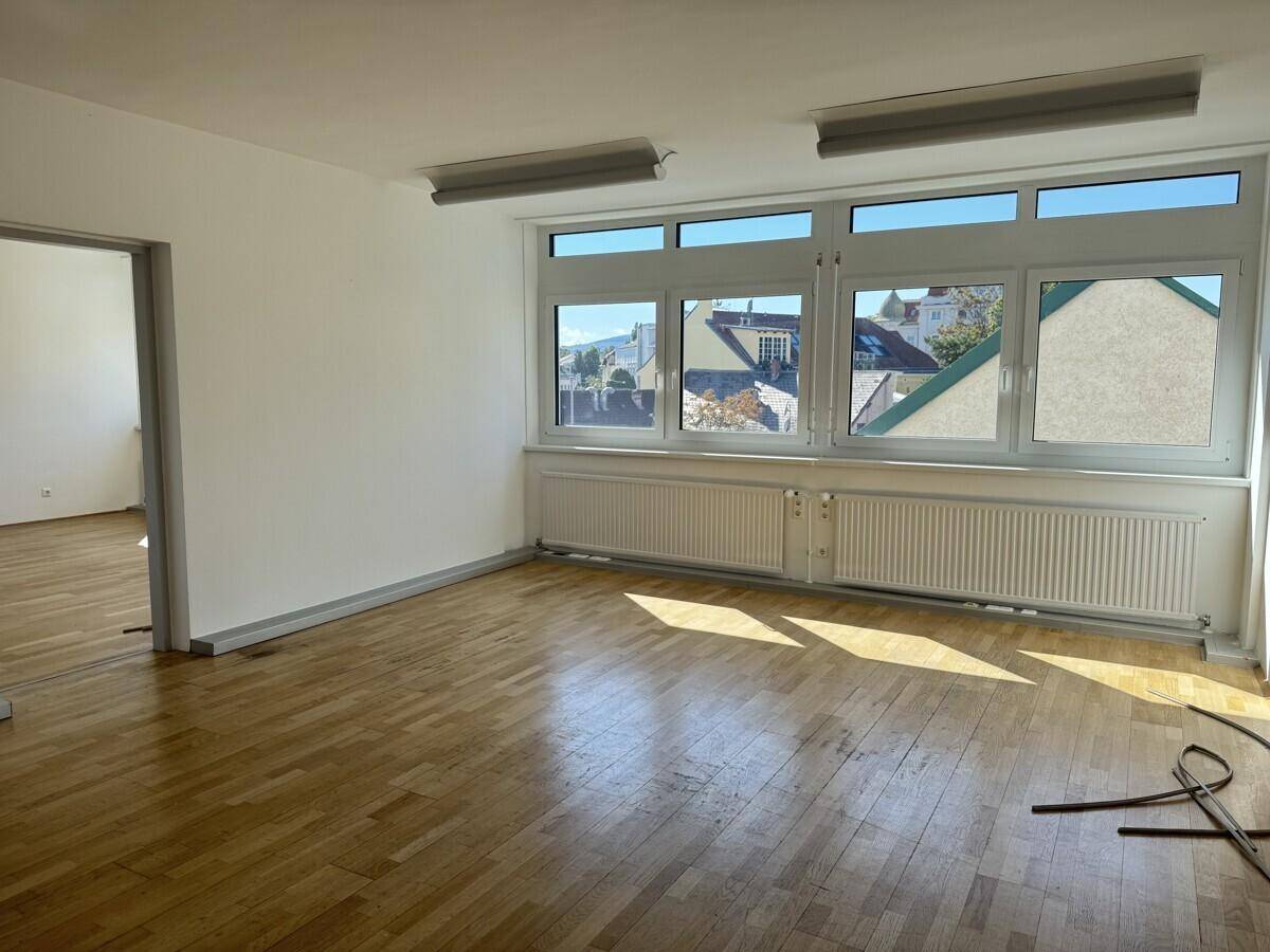 Geräumiger Büroraum mit Holzboden und großen Fenstern, die einen weiten Blick über die umliegenden Dächer ermöglichen.