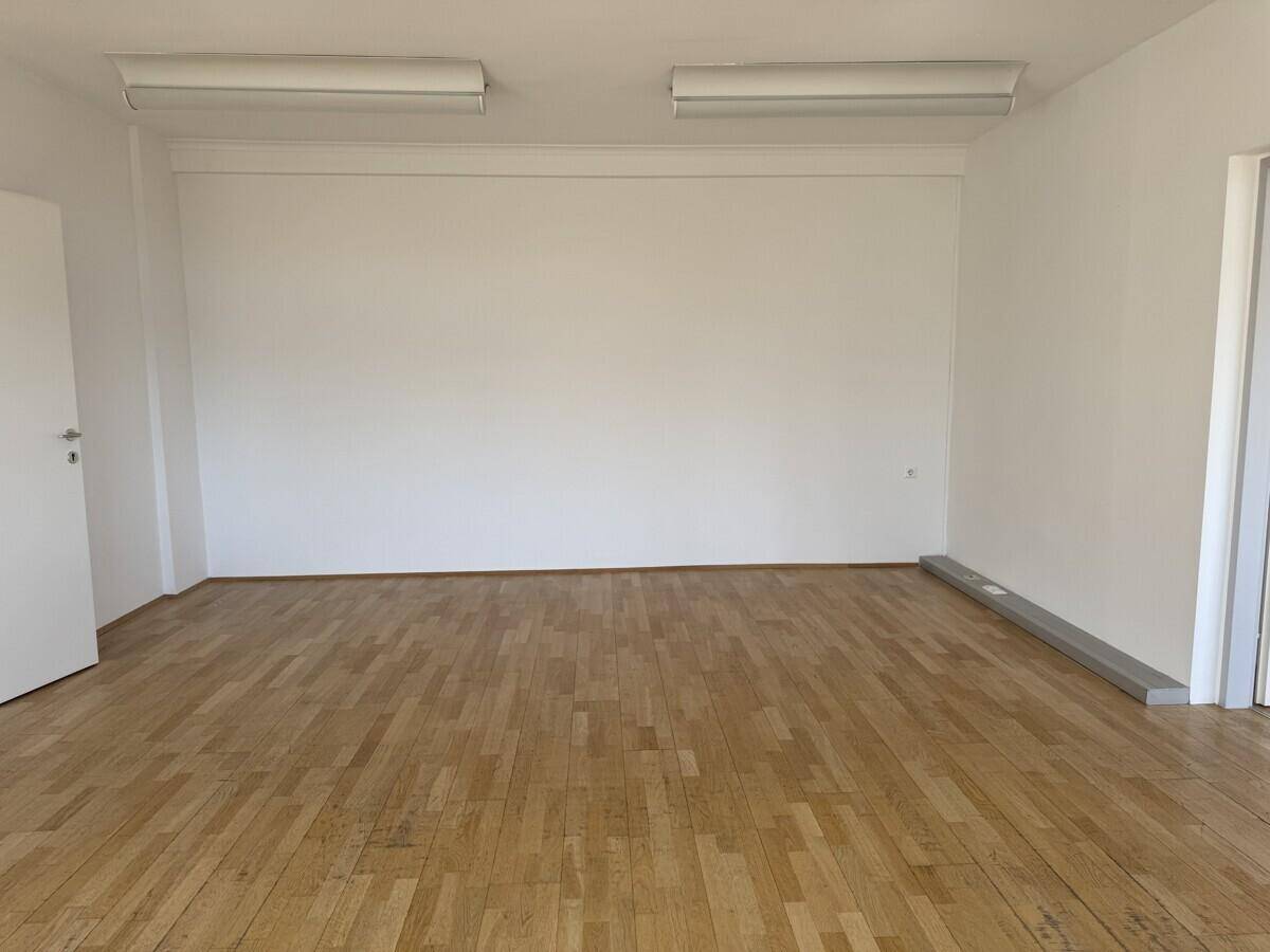 Schlichter, leerer Büroraum mit Holzboden und weißen Wänden, bereit für individuelle Gestaltung.