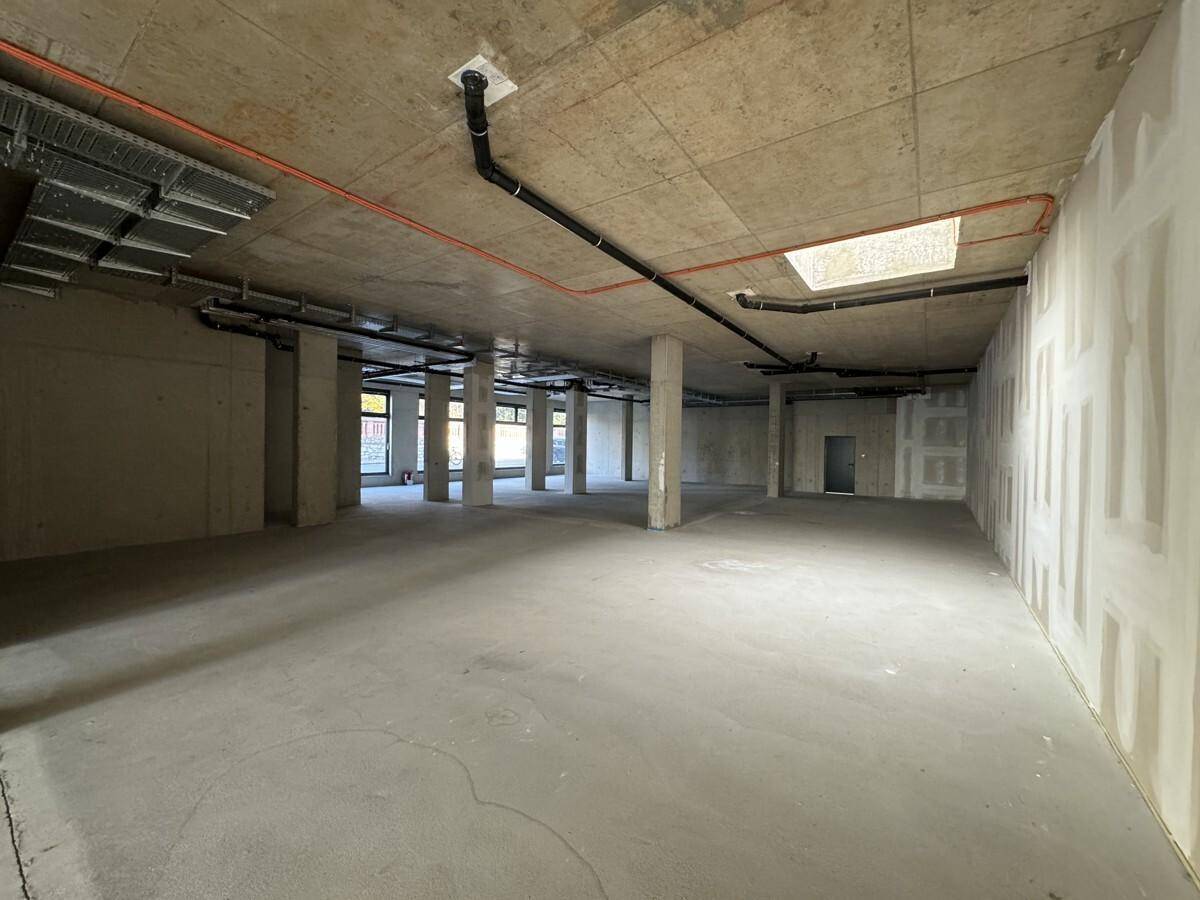 Weitläufiger, unfertiger Gewerberaum mit Betonboden, Säulen und sichtbaren Deckeninstallationen, ideal für flexible Gestaltung.