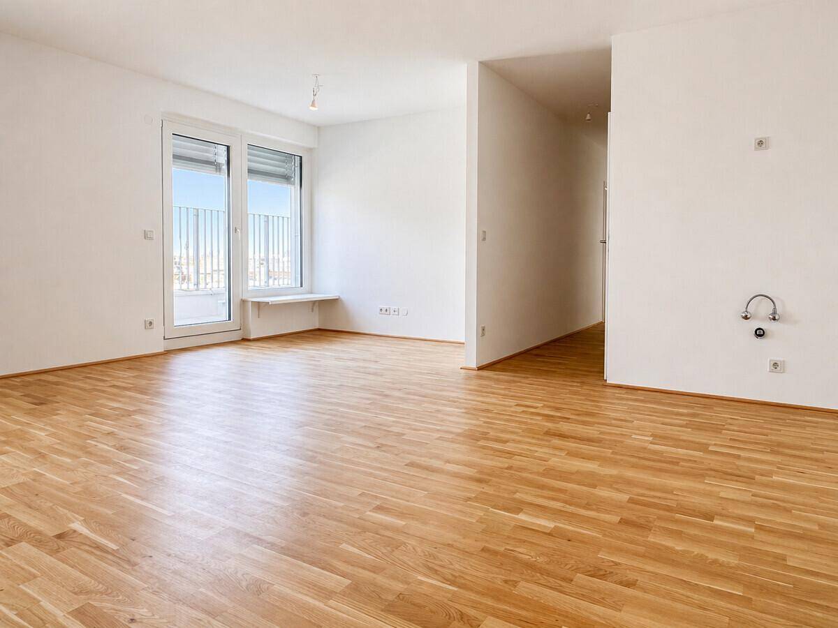 Geräumiges, helles Zimmer mit Holzboden und Blick auf die Umgebung durch die Balkontür.
