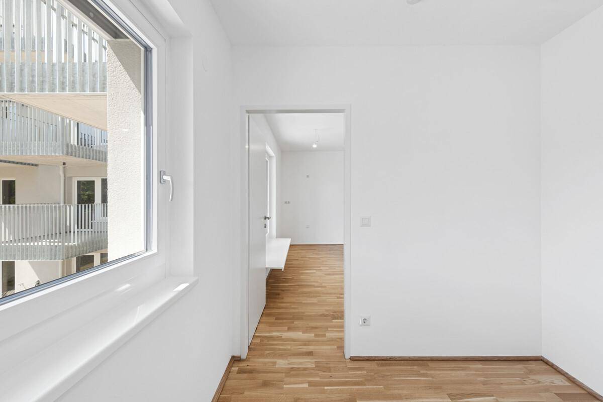Heller Flur mit Parkettboden und Zugang zu weiteren Räumen, mit Blick nach draußen.