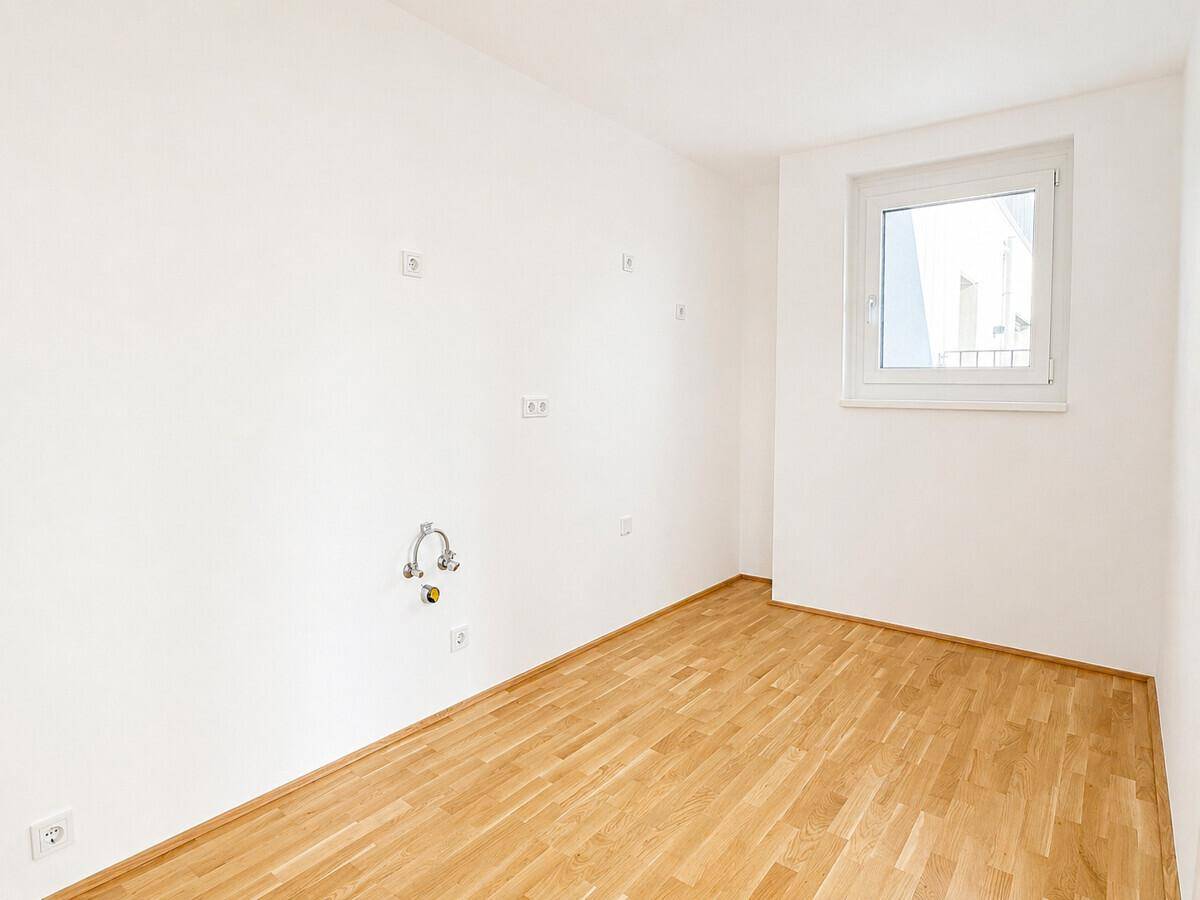 Leerer Raum mit Fenster und Anschlüssen für eine zukünftige, moderne Küche.