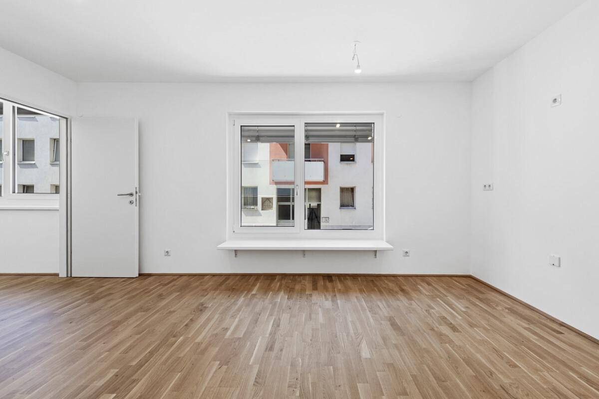 Geräumiges, helles Zimmer mit Parkettboden und Blick auf die gegenüberliegenden Gebäude.