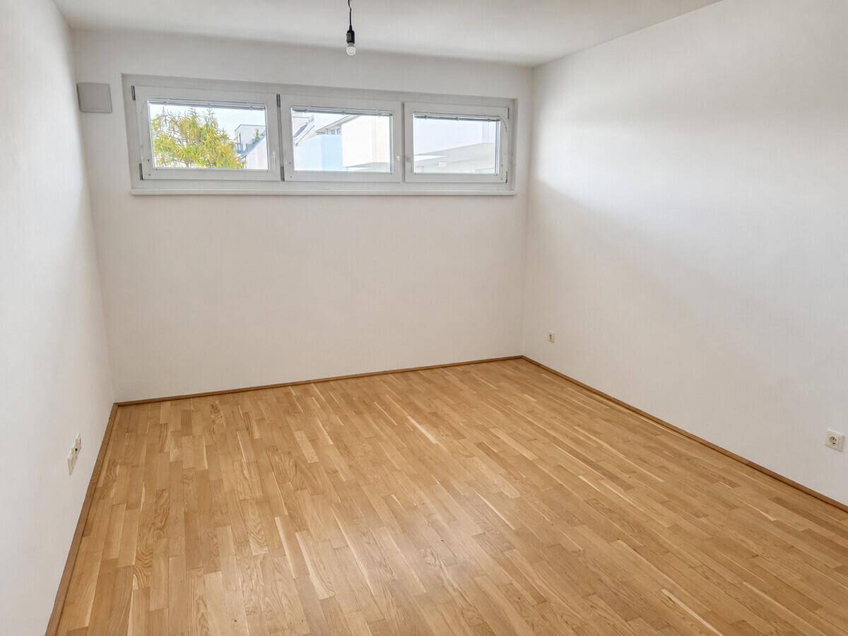 Helles Schlafzimmer mit Parkettboden und drei großen Fenstern, die viel Tageslicht hereinlassen.