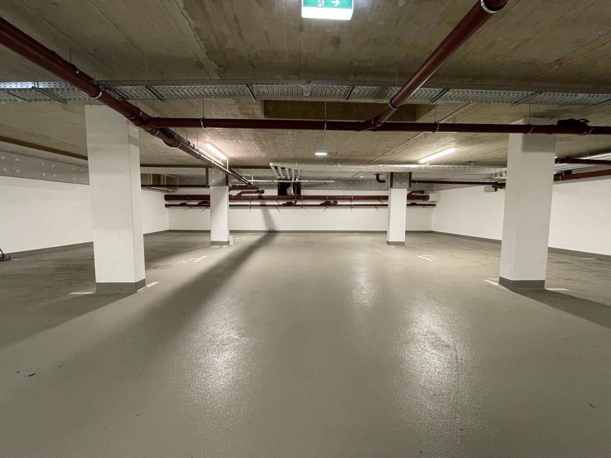 Geräumige Tiefgarage mit Betonwänden, Säulen und sichtbaren Rohrleitungen an der Decke.