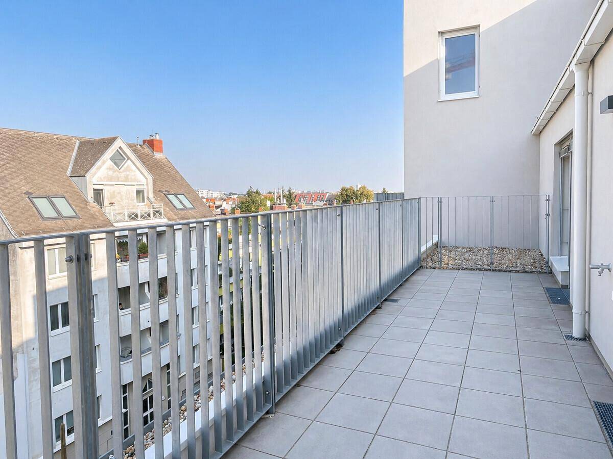 Geräumige Dachterrasse mit Fliesenboden und Metallgeländer, bietet einen Blick über die umliegenden Dächer.