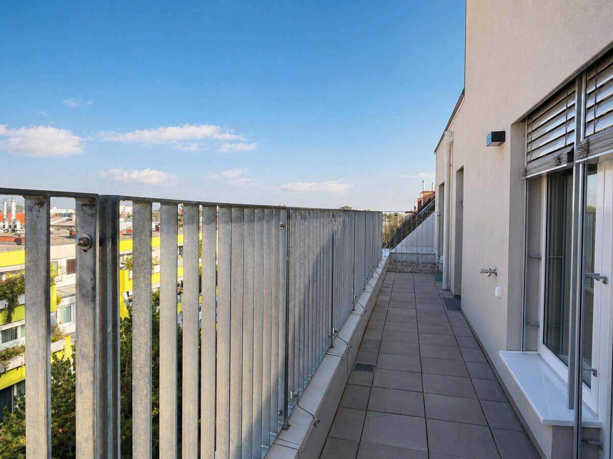 Langer, schmaler Balkon mit Metallgeländer und Blick auf die umliegenden Gebäude.