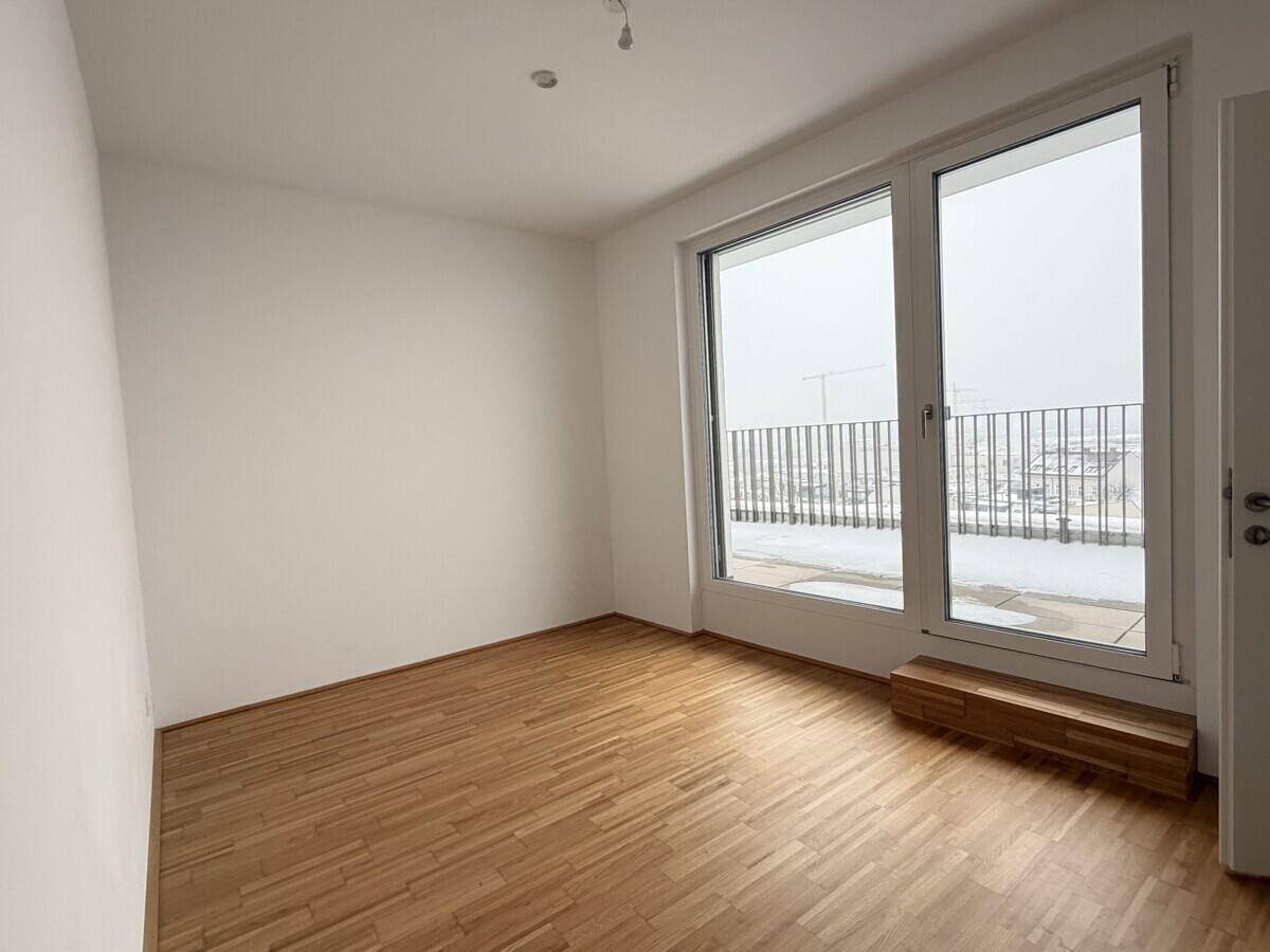 Helles Schlafzimmer mit Parkettboden und großem Fenster, das viel Tageslicht hereinlässt.