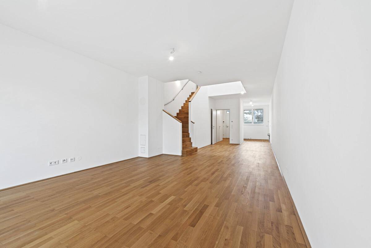 Helles, leeres Wohnzimmer mit neuem Parkettboden und offener Holztreppe zum Obergeschoss.
