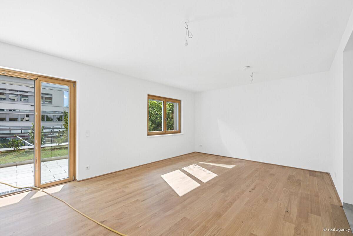 Geräumiger, heller Raum mit Holzboden und Zugang zu einer Terrasse oder einem Balkon.