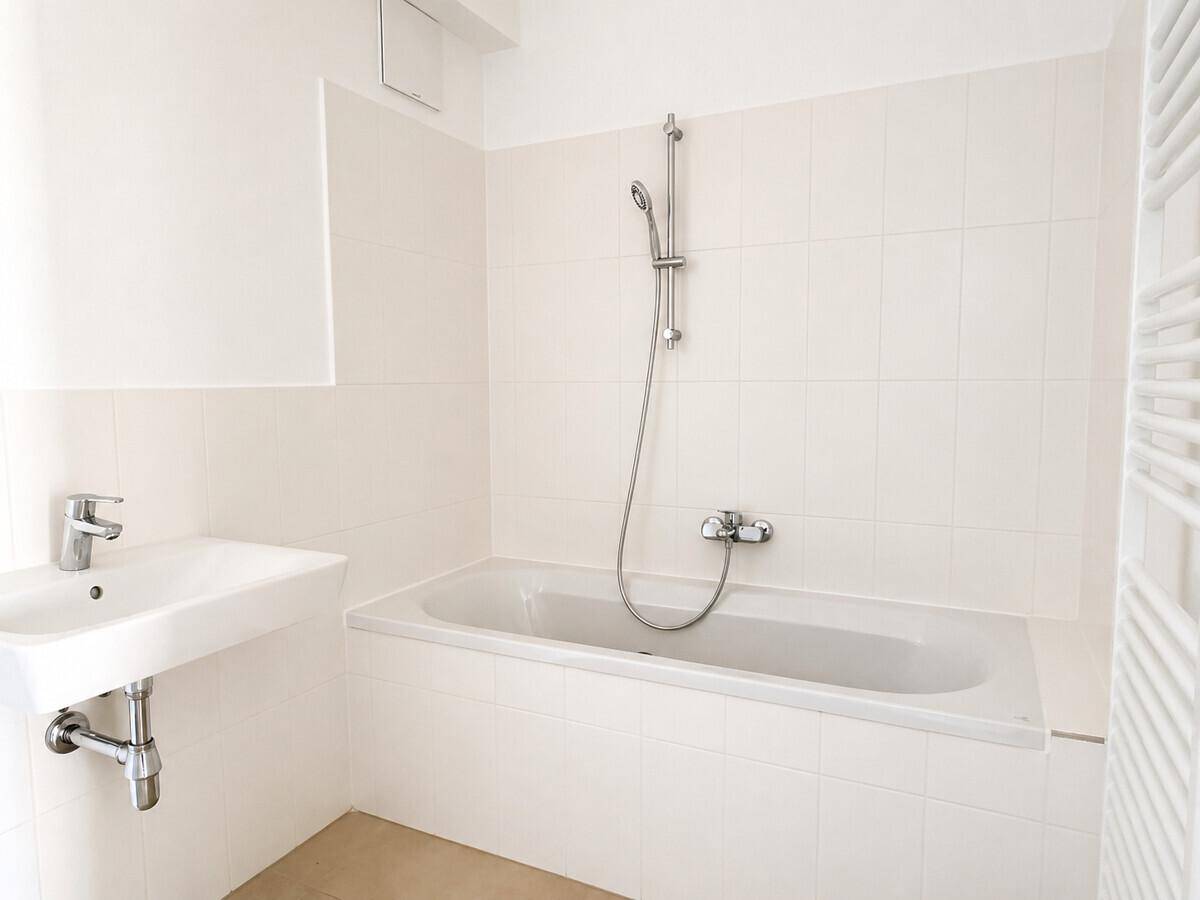 Modernes Badezimmer mit weißen Fliesen, Badewanne mit Duschfunktion und einem beheizten Handtuchhalter.
