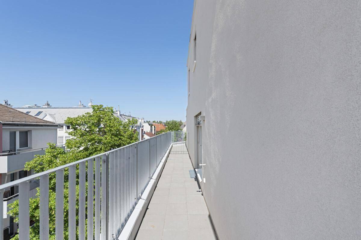 Langer Balkon mit Fliesenboden und Blick auf die umliegenden Gebäude und Bäume.