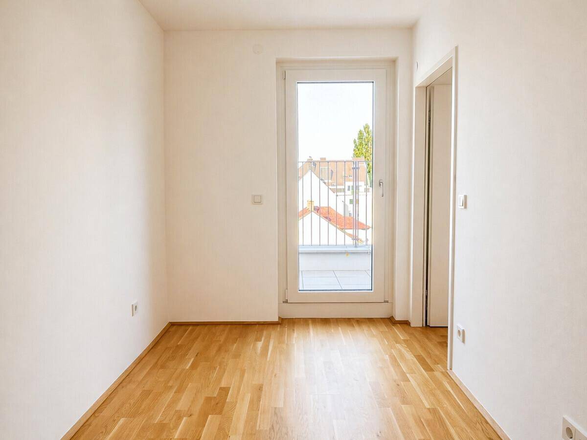 Kleineres Zimmer mit Parkettboden und Balkontür, bietet einen Blick auf umliegende Dächer.