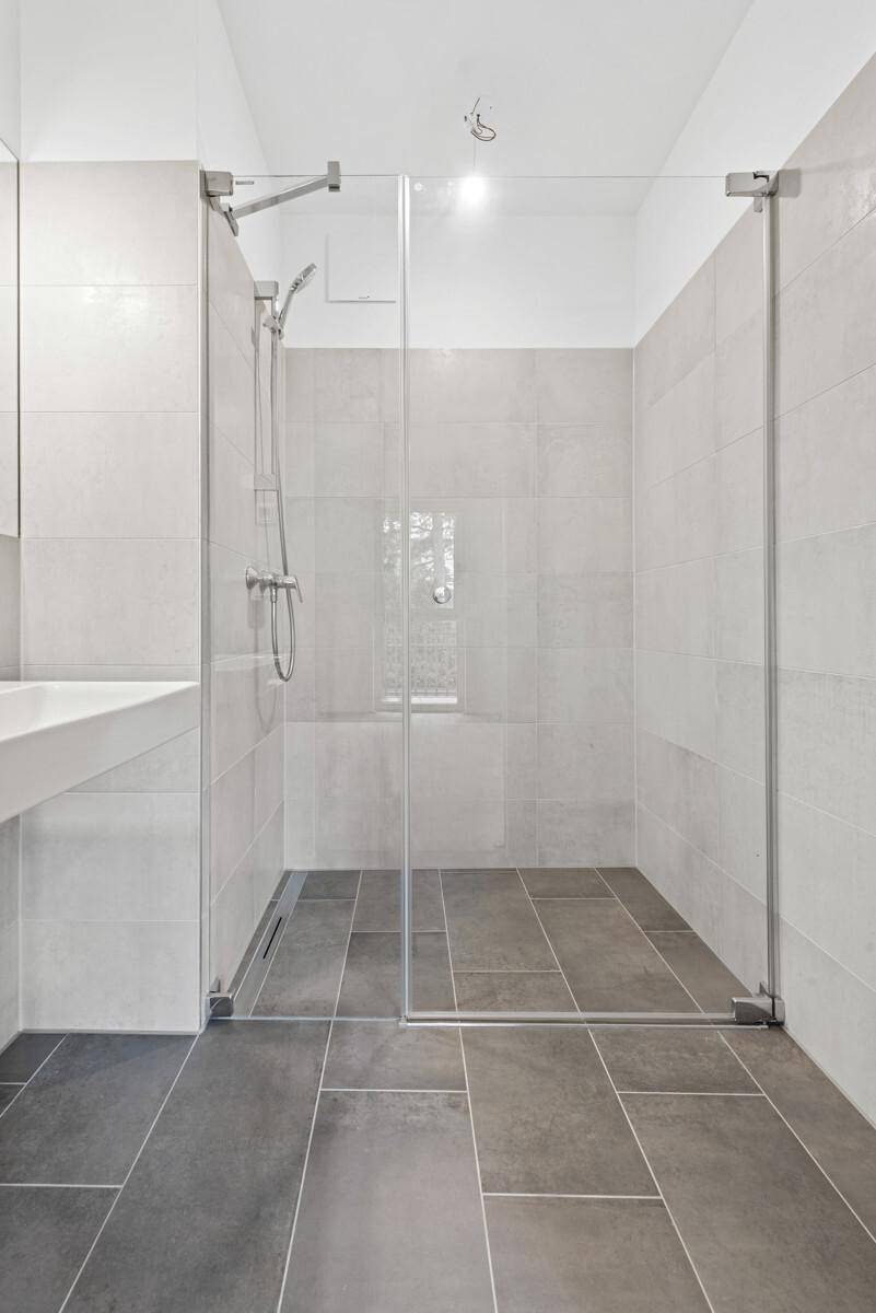 Modernes Badezimmer mit ebenerdiger Dusche, Glasabtrennung und großformatigen Fliesen.