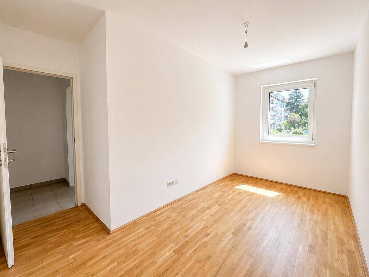 Helles Zimmer mit Parkettboden und Fenster, das einen Blick auf die Umgebung bietet.