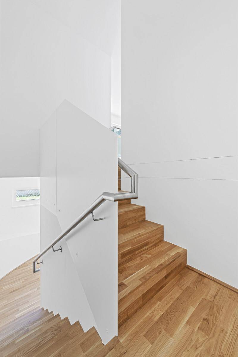 Elegante Holztreppe mit modernem Glasgeländer und Edelstahlhandlauf in hellem Ambiente.