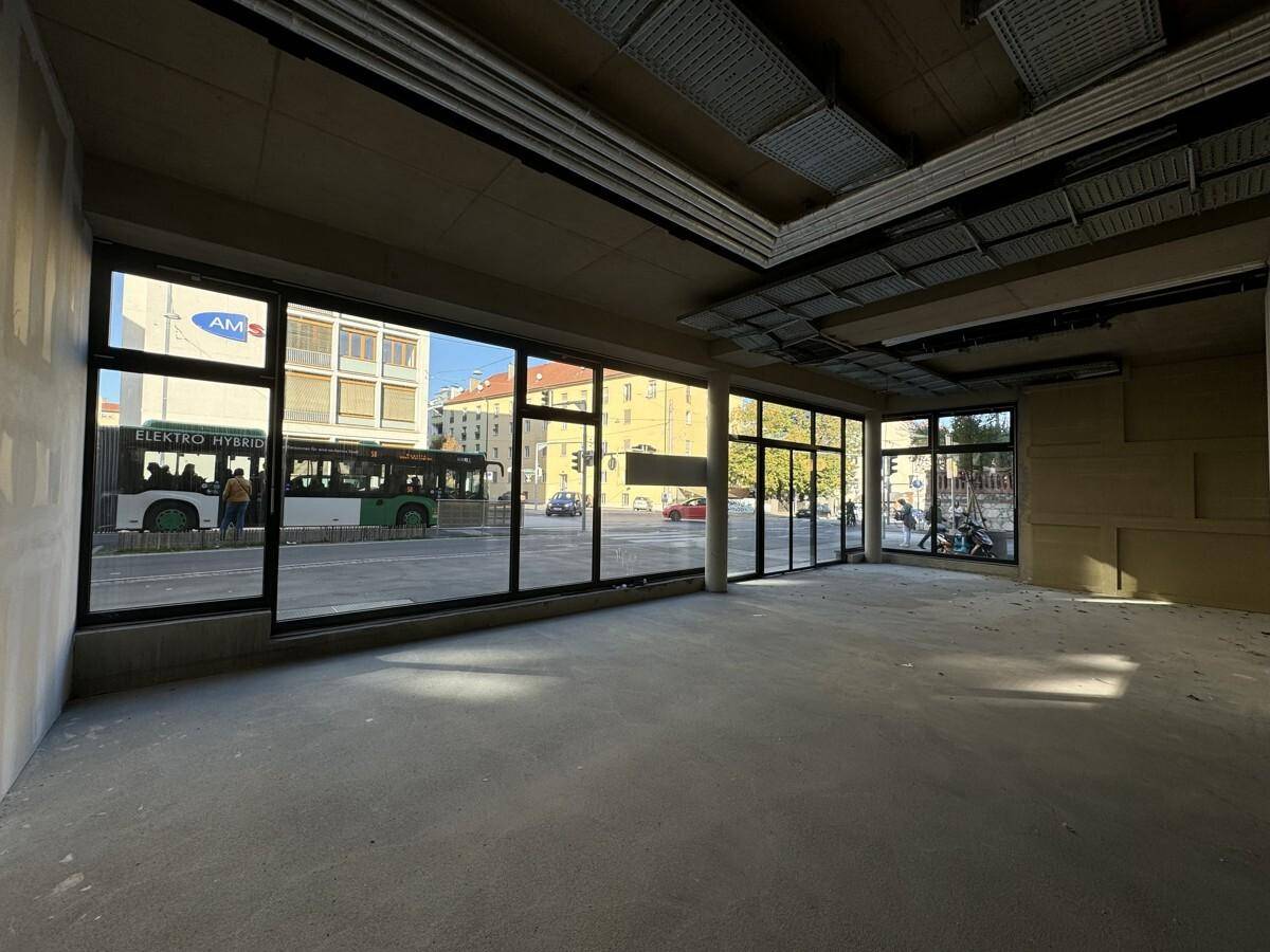 Heller Gewerberaum im Rohbau mit großen Fensterfronten zur belebten Straße und Betonboden.