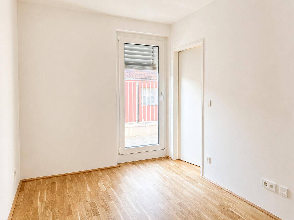 Kleineres, helles Zimmer mit Parkettboden und Zugang zu einem Außenbereich, ideal als Schlafzimmer.