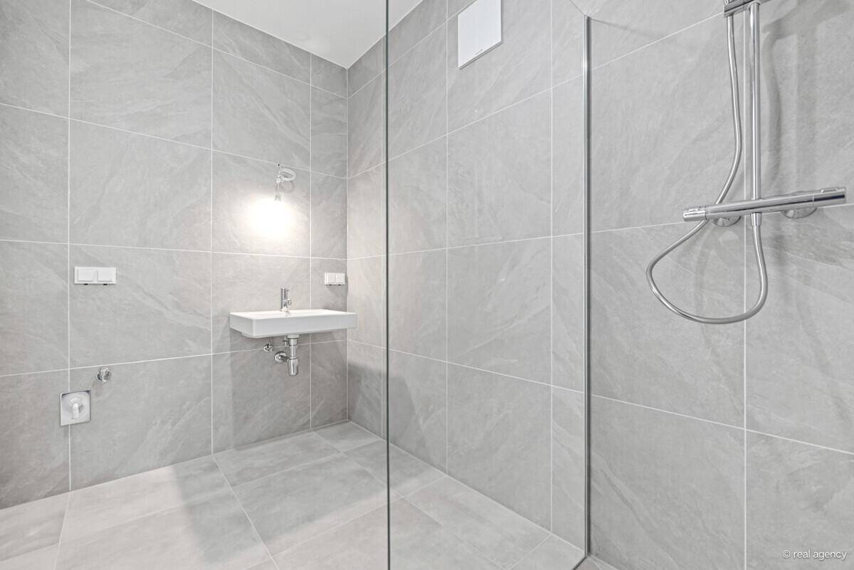 Modernes Badezimmer mit grauen Fliesen, Einzelwaschbecken und einer begehbaren Dusche.